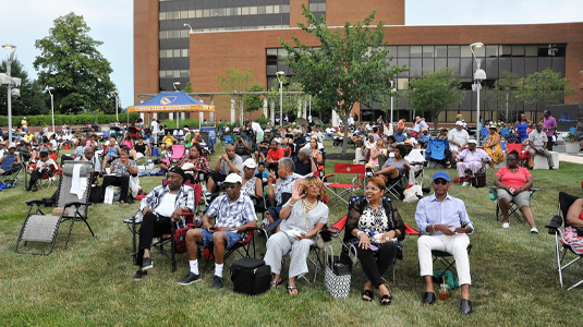 一大群不同的人坐在科平校园大楼前草地上的椅子上。