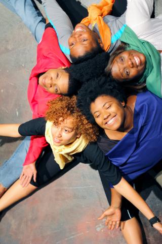 5褐色皮肤的年轻女性每个穿着一件色彩鲜艳的衬衫坐在开着伸着胳膊和紧密组合在一起
