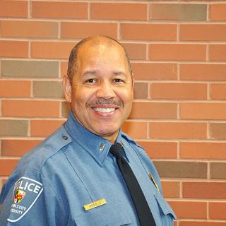 褐色皮肤穿着蓝色警察制服的男人微笑着站在面前red-ish砖墙