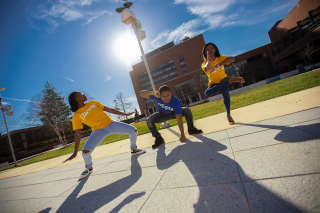 学生们穿着蓝色和黄色的Coppin衬衫，在阳光明媚的日子里摆出戏剧性的姿势
