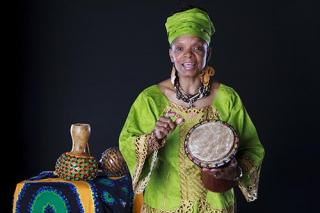 一位穿着彩色非洲服装和珠宝的资深非裔美国人讲故事的人。她拿着非洲鼓，正在讲故事。