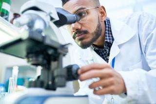 男学生在化学实验室做研究时对着显微镜看。