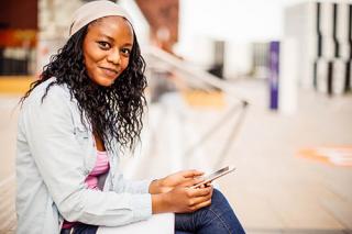 年轻学生坐在大学门口使用智能手机的照片