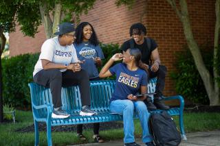 四名学生在Coppin校园的蓝色长凳上聊天